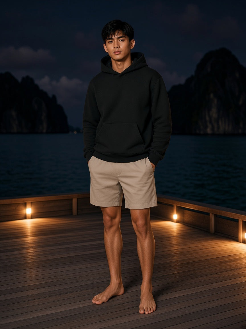 Marcel Afters Fleece Regular Shoulder Hoodie in Black, worn by a man, standing barefoot on a lit jetty at night
