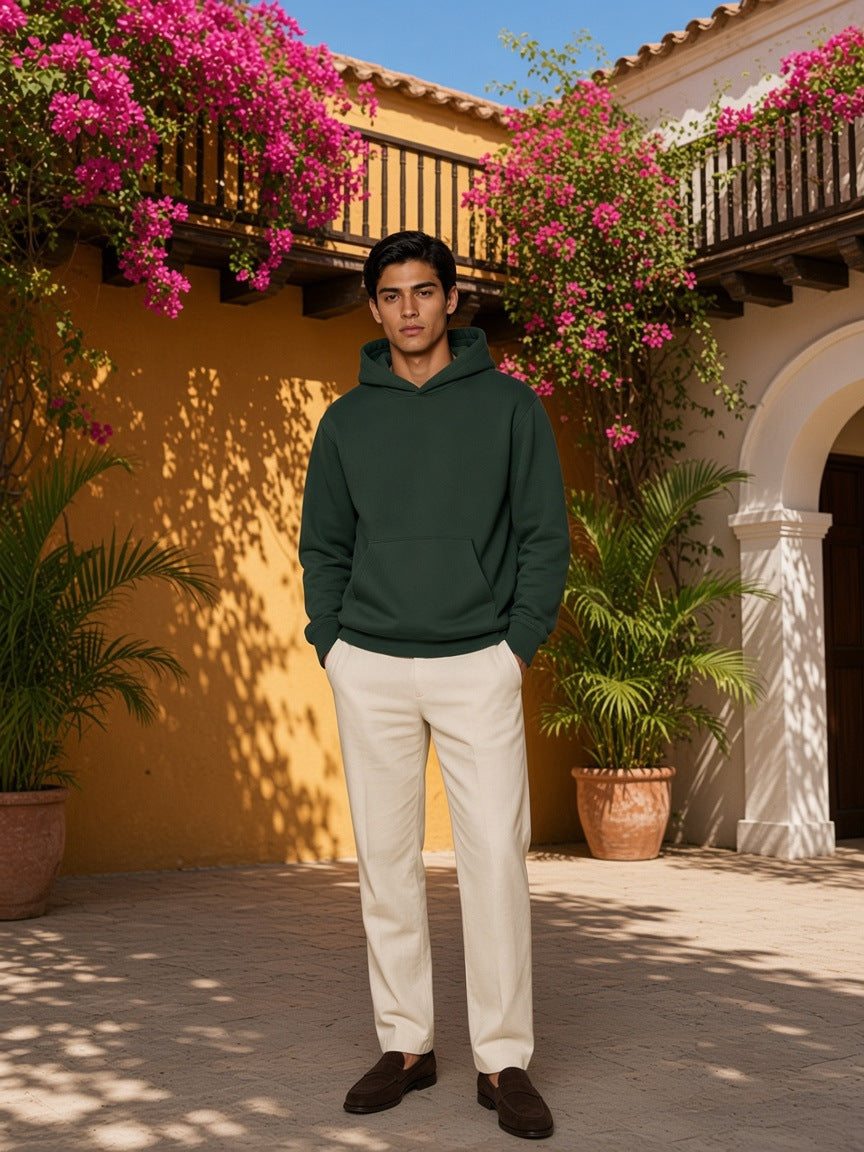 Marcel Afters Fleece Regular Shoulder Hoodie in Dark Green, worn by a man, standing in a sunlit courtyard with bougainvillea