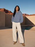 Marcel Afters Frayed Enzyme Washed Fleece Hoodie in Blue, worn by a woman, standing by a desert courtyard pool in wide cream trousers