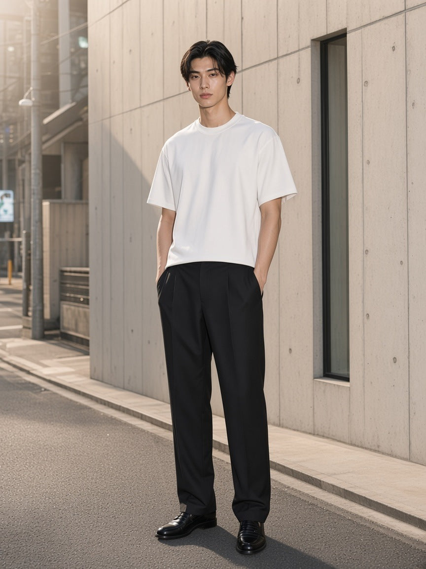 Marcel Afters French Terry Raw Edge T-Shirt in White, worn by a man, standing by a concrete wall on a quiet street in black trousers
