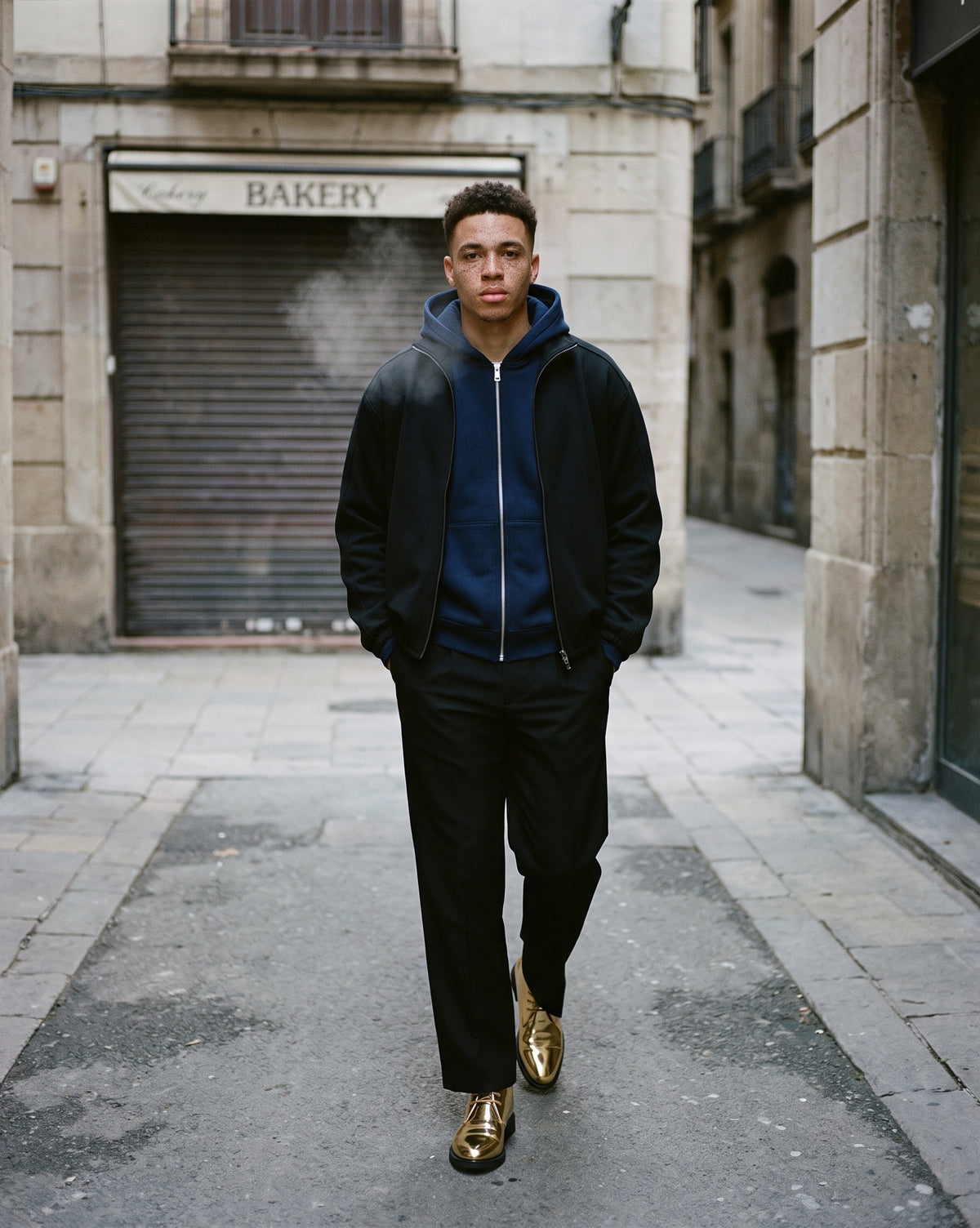 Man wearing The Encore Boot with the Men's Heavyweight Full Zip Hoodie in Navy Blue, Adjustable Waist Straight-Leg Trousers in Black, Heavyweight Stand Collar Jacket in Black. Cold City, Autumn–Winter 2026 campaign