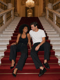 Marcel Afters Heavyweight Cotton Straight-Leg Pants in Black, worn by a man and a woman, seated together on a red-carpeted grand staircase