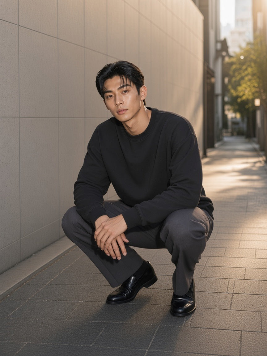 Man in the Heavyweight Drop Shoulder Sweatshirt in Black Beauty with charcoal trousers and loafers, in a stone alley in Aoyama, Tokyo in the morning