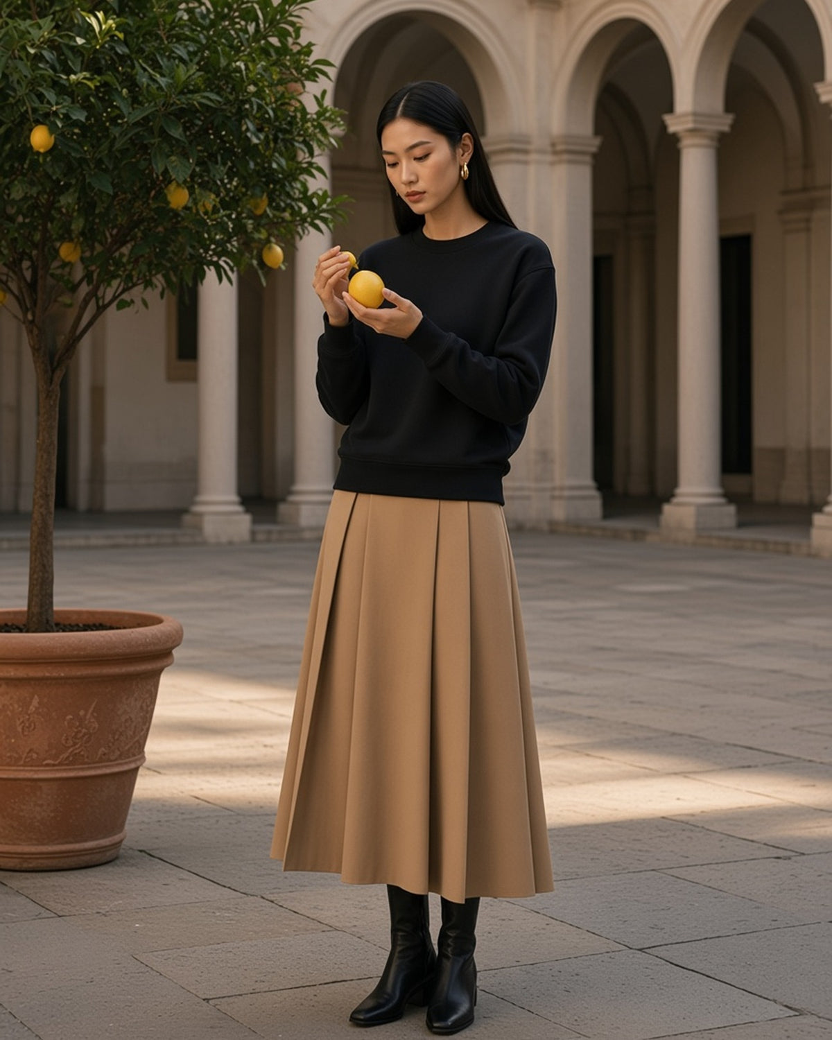 Woman in the Heavyweight Drop Shoulder Sweatshirt in Black Beauty, with a lemon in a Milan palazzo courtyard