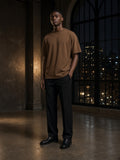 Marcel Afters Heavyweight Drop Shoulder T-Shirt in Coffee, worn by a man, standing in a dim hall with city lights in arched windows