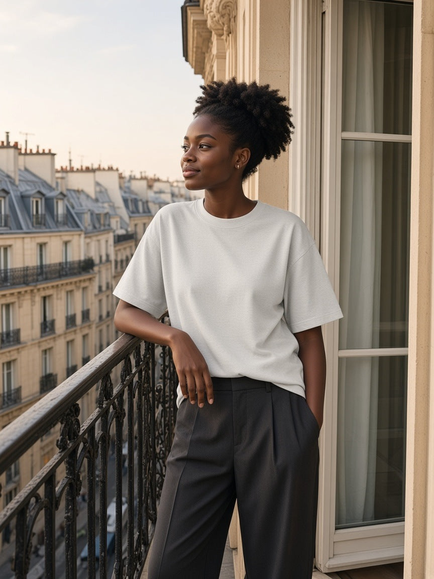 Woman in the Heavyweight Drop Shoulder T-Shirt in Oat Gray on a Paris balcony above the zinc roofs in the morning