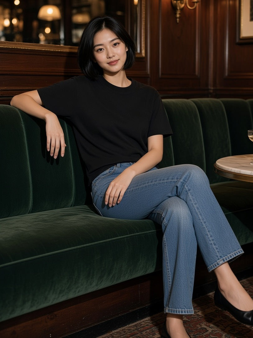 Woman in the Heavyweight Earth Tone T-Shirt in Black on a green velvet banquette in a Paris hotel bar after hours