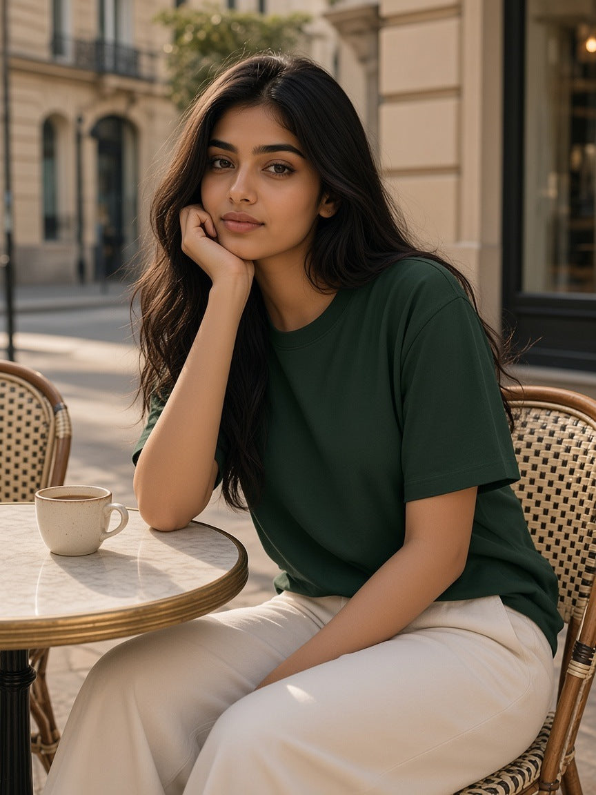 Woman in the Heavyweight Earth Tone T-Shirt in Blackish Green at a marble café table on a Paris pavement