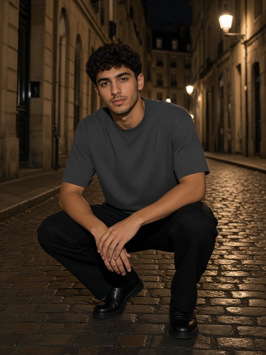 Man in the Heavyweight Earth Tone T-Shirt in Carbon Gray crouched on wet Marais cobblestones at night