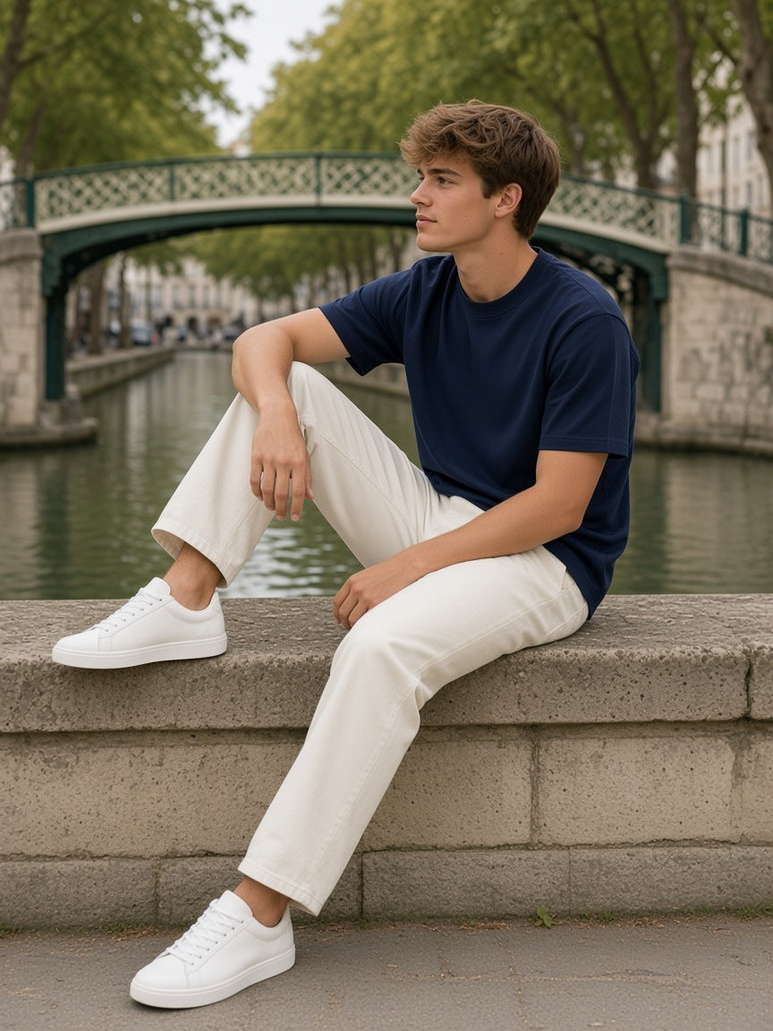 Man in the Heavyweight Earth Tone T-Shirt in Navy sitting on a stone ledge by the Canal Saint-Martin, Paris