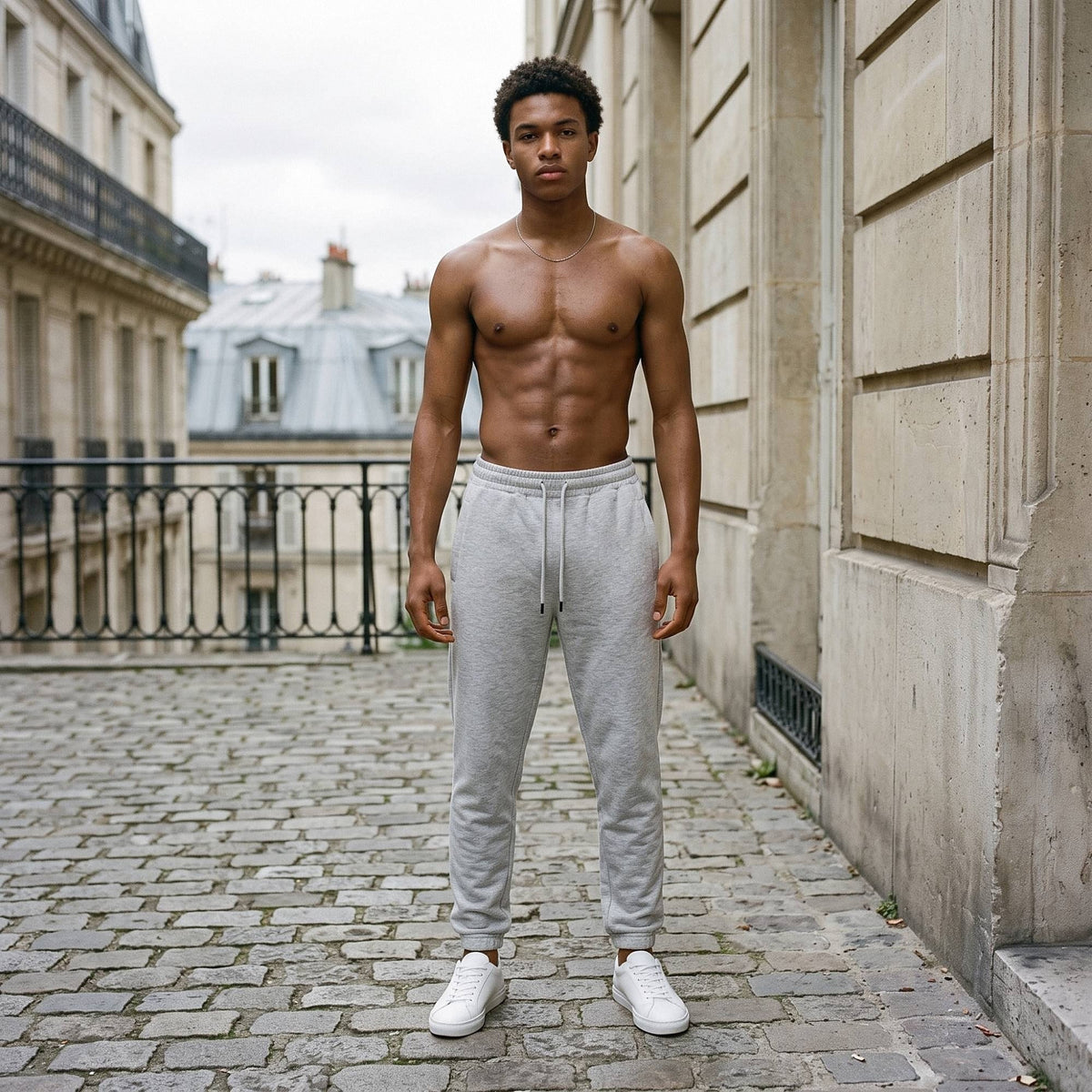 Shirtless man in the Men's Heavyweight Fleece Joggers in Flower Gray on Paris cobbles, zinc roofs behind