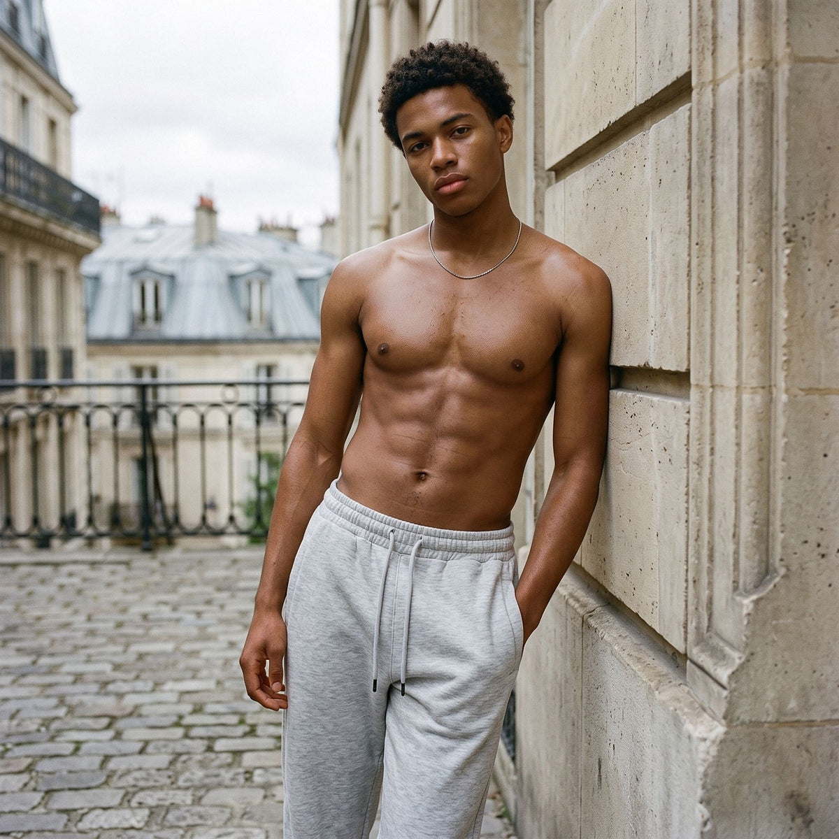 Shirtless man in the Men's Heavyweight Fleece Joggers in Flower Gray leaning on a limestone wall in Paris