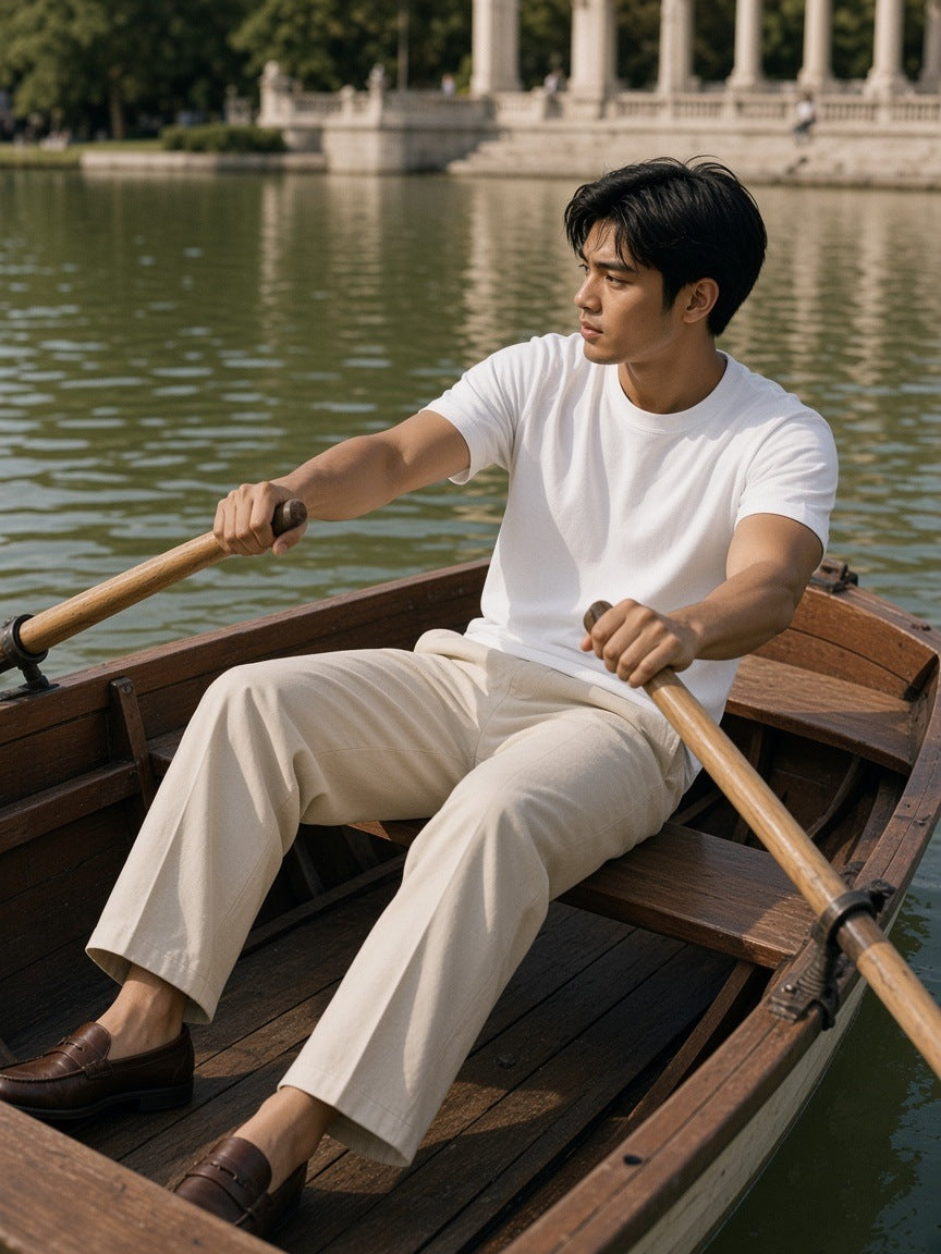 Man in the Men's Heavyweight Earth Tone T-Shirt in White with stone pleated trousers, rowing a boat on the Retiro lake in Madrid