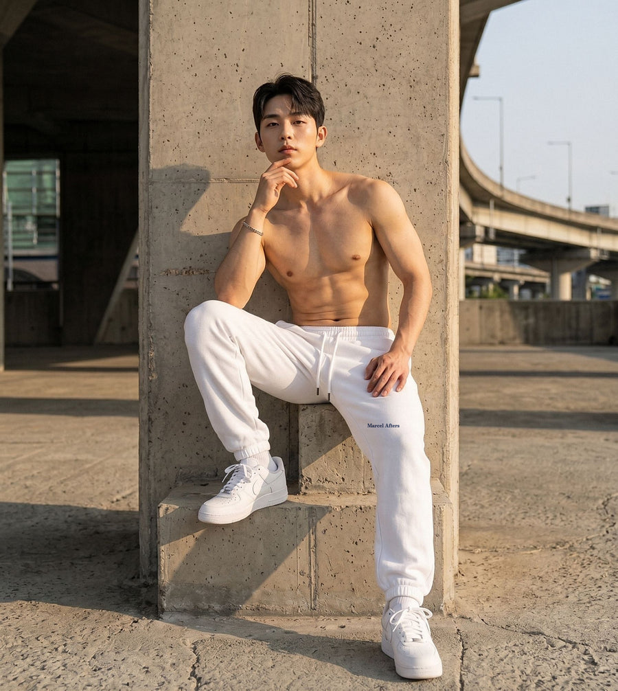 Man in white Marcel Afters heavyweight fleece joggers seated on a concrete ledge, wordmark at the left hip