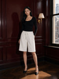 Marcel Afters Heavyweight Fleece Loose Fit Shorts in Lucent White, worn by a woman, standing in a wood-panelled bar in wide white shorts and a black top