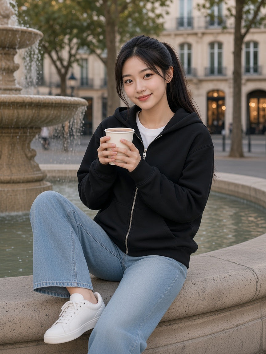 Woman in the Heavyweight Full Zip Hoodie in Black on the edge of a fountain in a Paris square at dusk