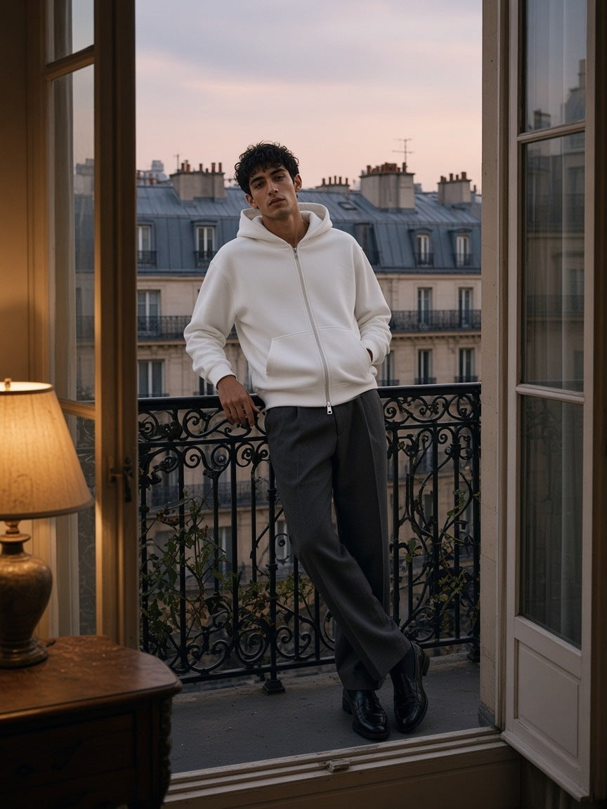 Man in the Heavyweight Full Zip Hoodie in White on a Haussmann balcony above the Paris rooftops at dusk