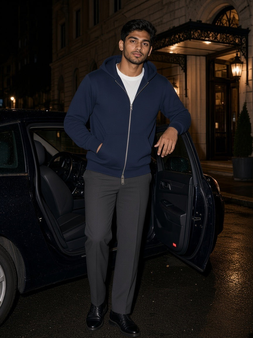 Man in a Navy Blue heavyweight full zip hoodie beside a car outside a grand hotel at night