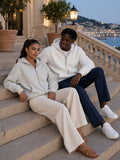Two people in the Heavyweight Full Zip Hoodie in Oat Gray and White, sitting on the steps of a Nice hotel terrace at blue hour