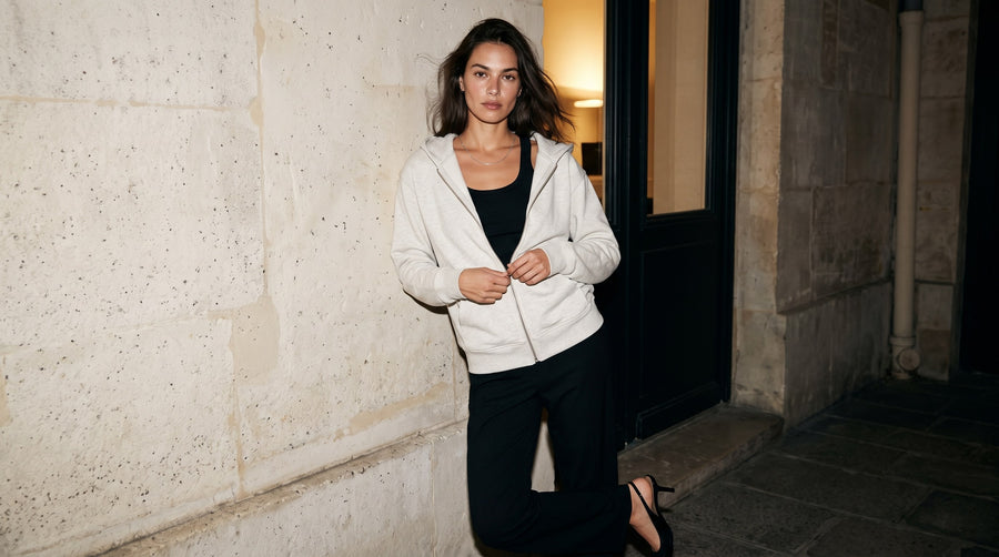 Woman in the Marcel Afters Heavyweight Full Zip Hoodie in Oat Gray, zipped over a black top and trousers at a Paris doorway
