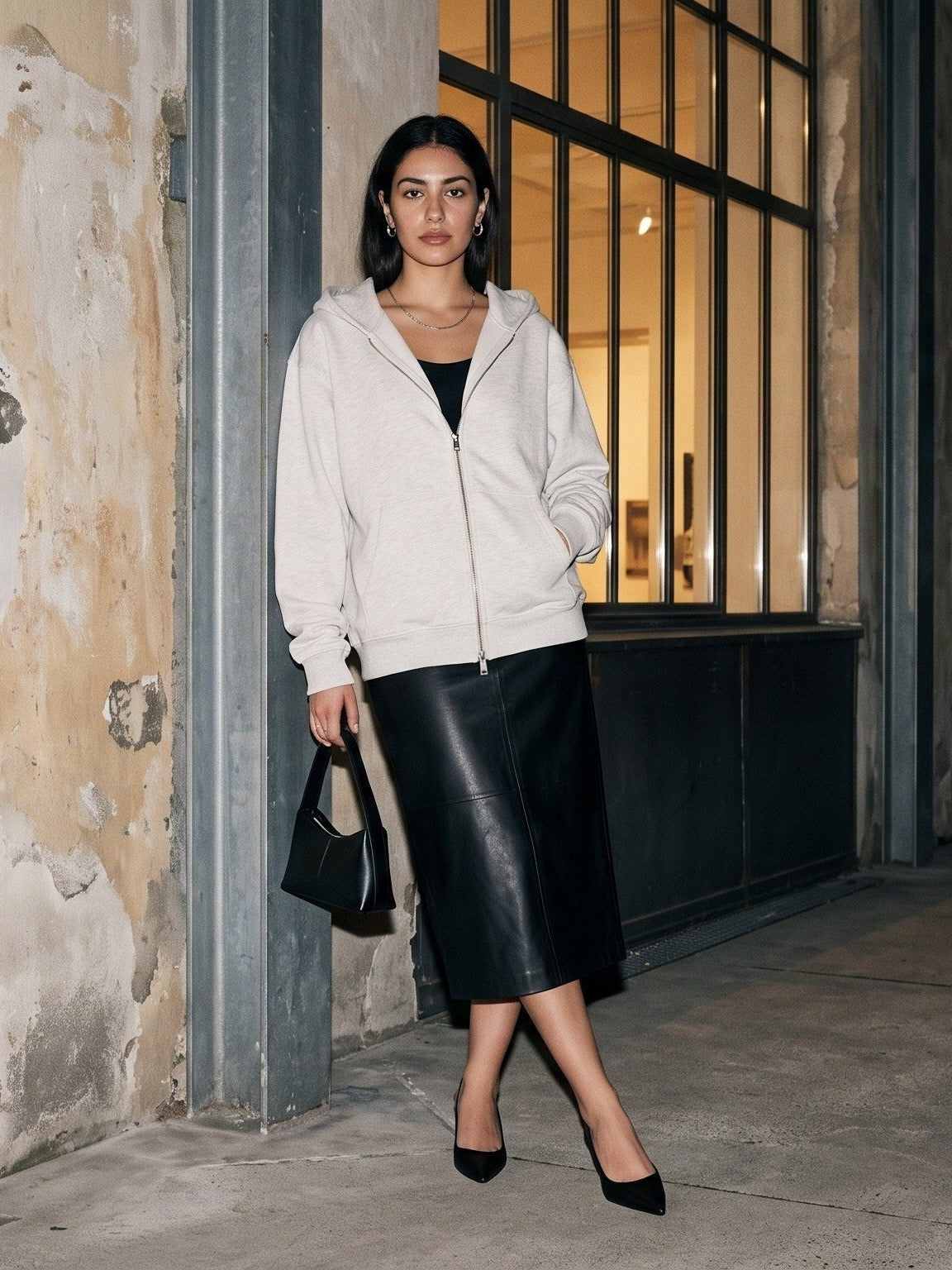 Woman in the Heavyweight Full Zip Hoodie in Oat Gray worn with a black leather midi skirt and heels outside a Paris gallery