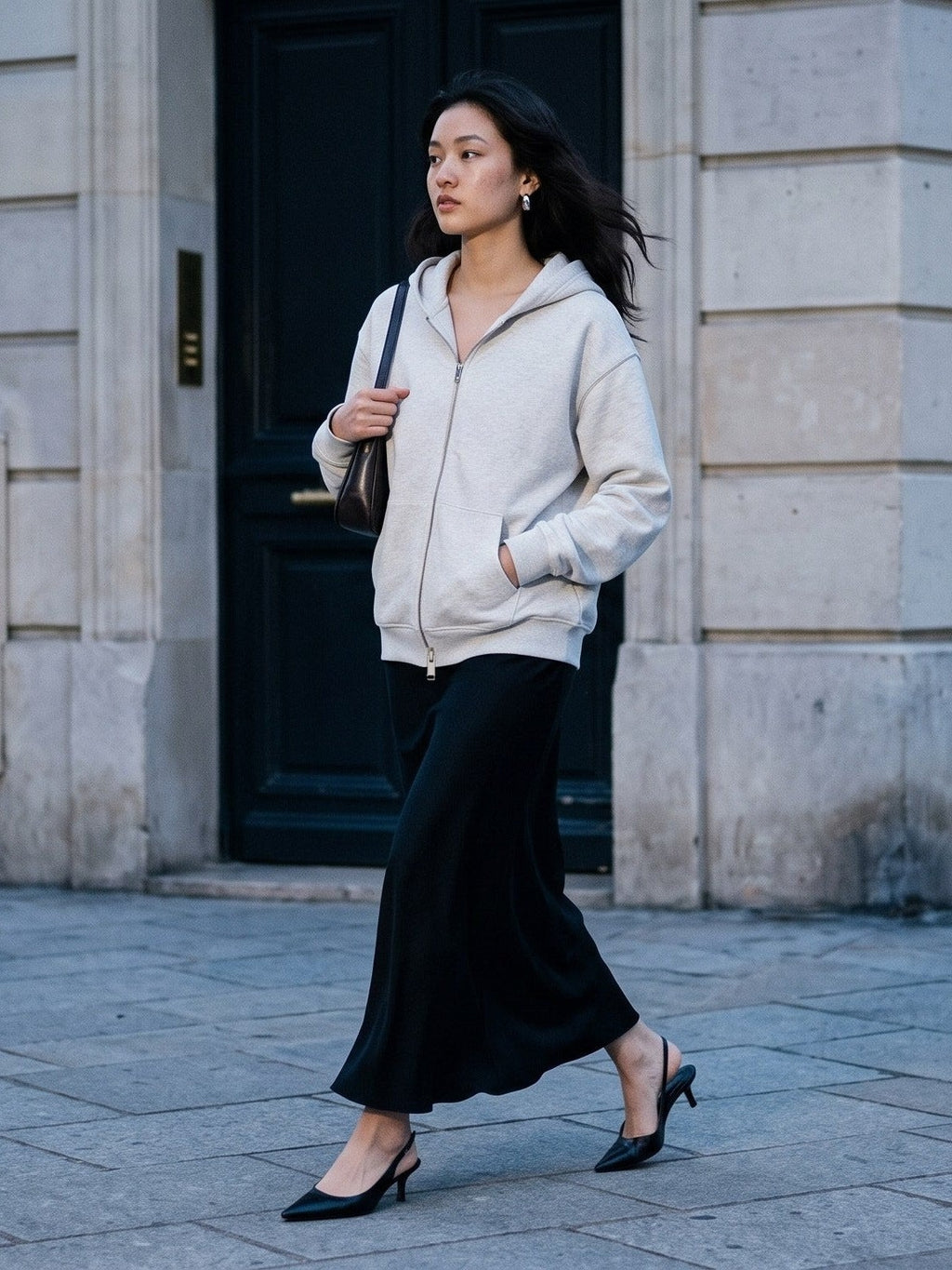 Woman in the Heavyweight Full Zip Hoodie worn with a long black skirt and slingback heels crossing a blue-grey Paris street