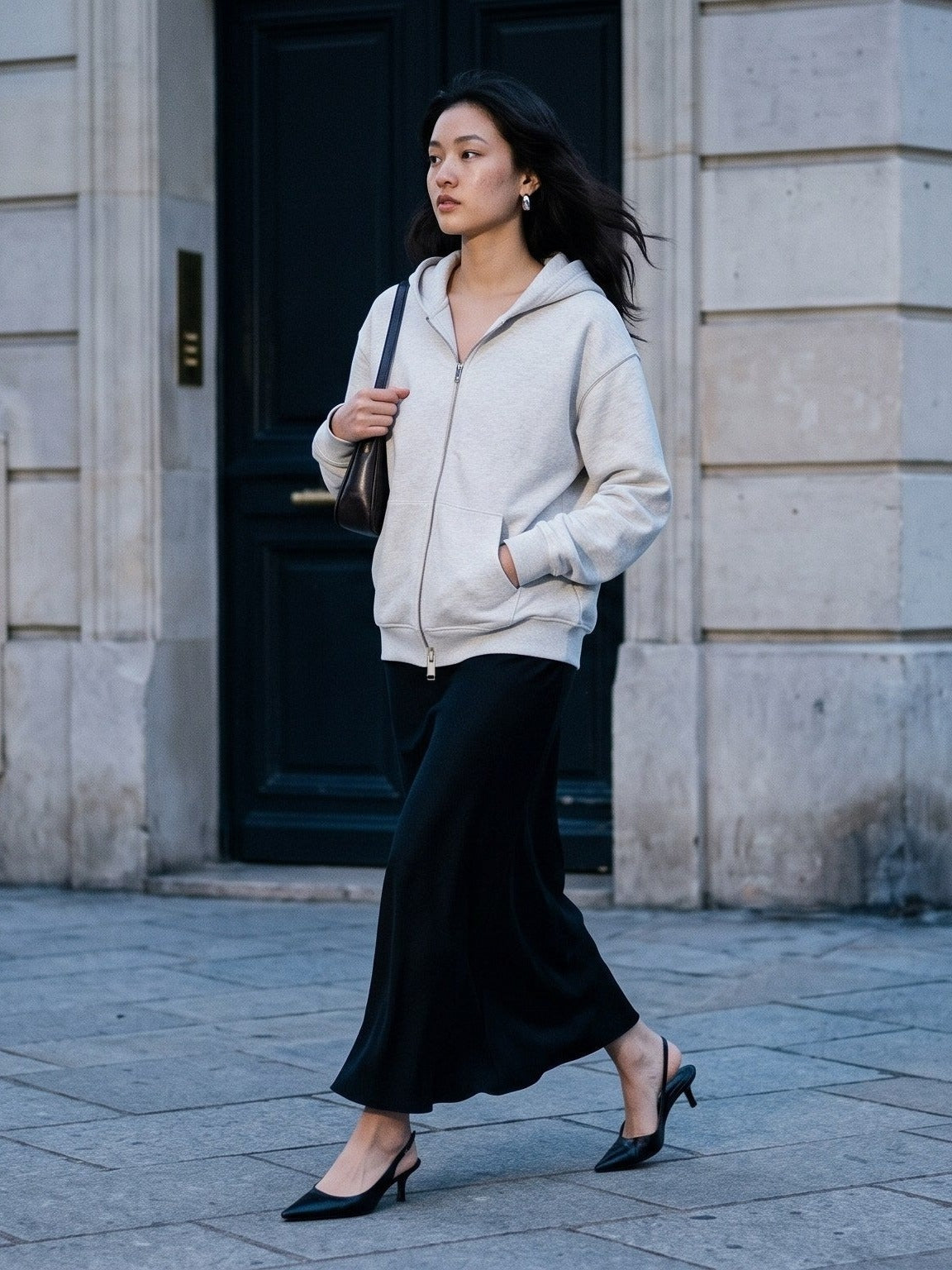 Woman in the Heavyweight Full Zip Hoodie worn with a long black skirt and slingback heels crossing a blue-grey Paris street