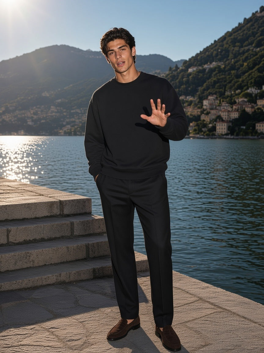 Marcel Afters Heavyweight Oversized Boxy Sweatshirt in Black, worn by a man, standing on lakeside stone steps in the afternoon sun