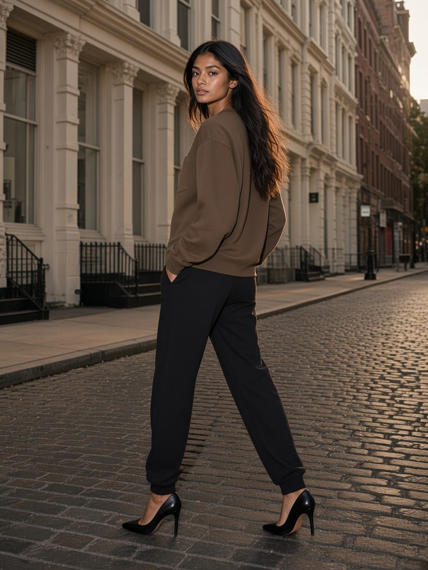 Marcel Afters Heavyweight Patch Pocket Crewneck Sweatshirt in Coffee, worn by a woman, walking a cobbled street in black joggers and heels