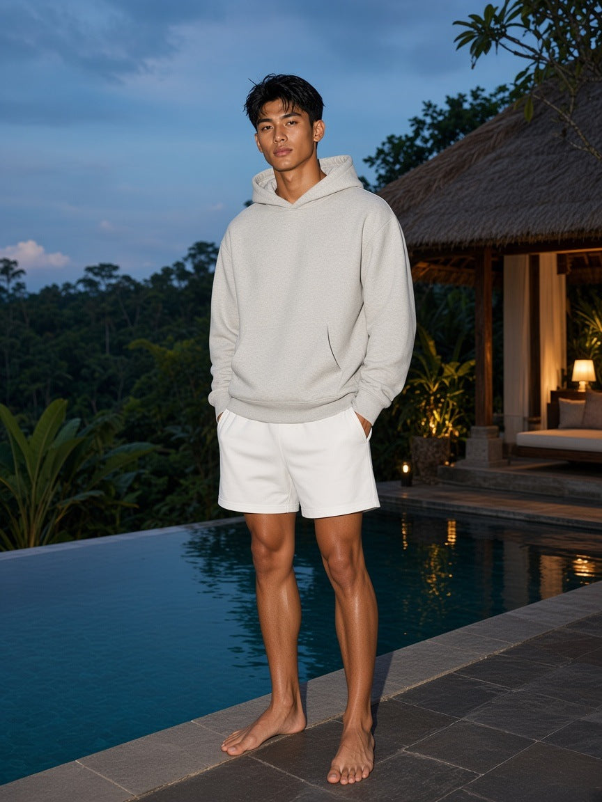 Marcel Afters Heavyweight Pullover Hoodie in Oat Gray, worn by a man, standing barefoot by an infinity pool at dusk