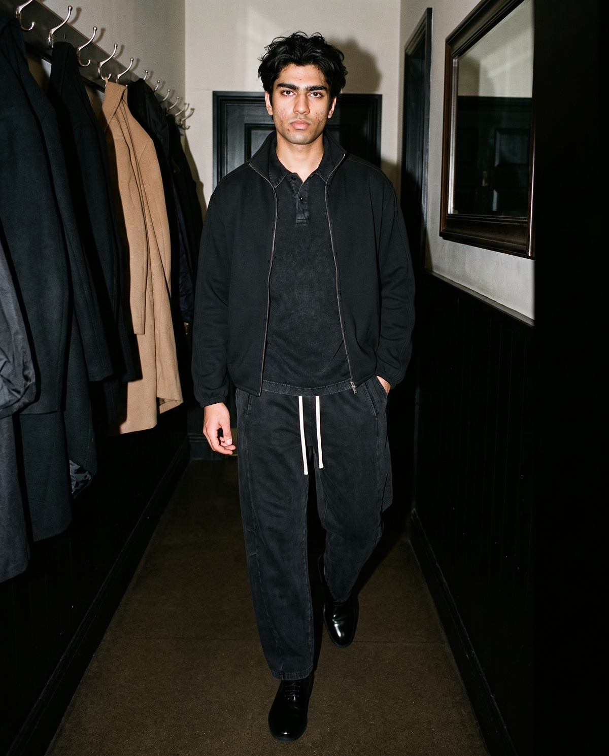 Man in Black heavyweight snow-washed polo under a black zip jacket, in a hallway