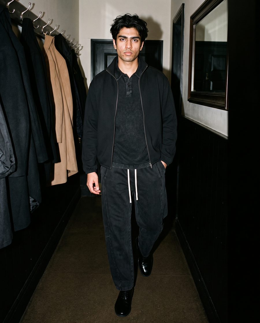 Man in Black heavyweight snow-washed polo under a black zip jacket, in a hallway