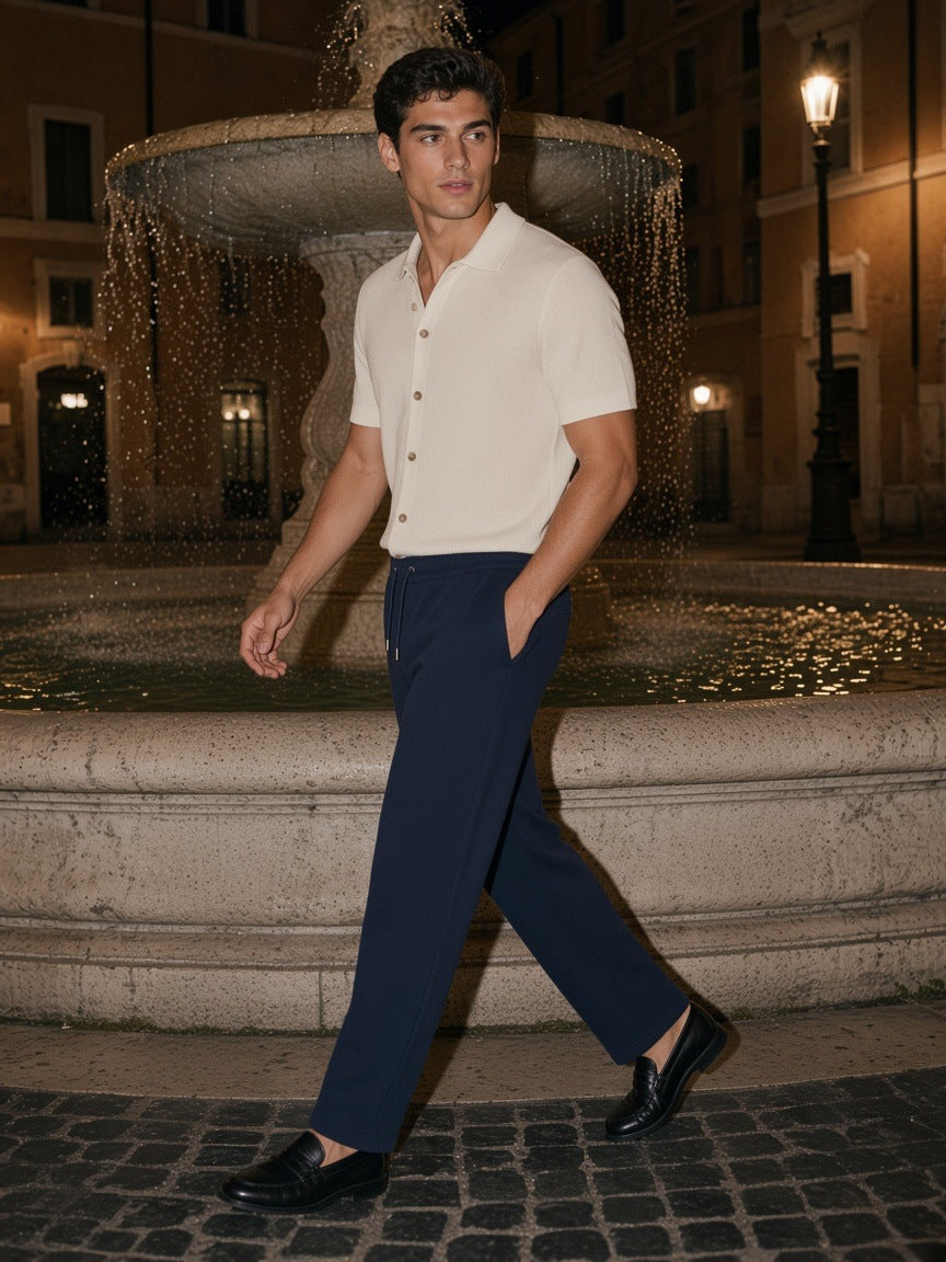 Man in the Heavyweight Sweatpants in Navy Blue walking past a fountain in a piazza in Rome at night