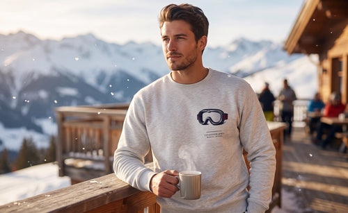 I Stayed For Après crewneck worn on a sunny chalet terrace with a coffee, mountains behind: après-ski in Aspen, Park City or the Alps.