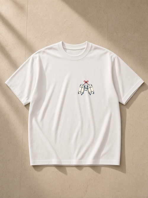 Leaned Together heavyweight tee in White, front view with two suitcases and a vanity case tied with a red bow. Marcel Afters.
