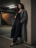 Woman in black lightweight tapered track pants and a charcoal overcoat in a concrete car park at night