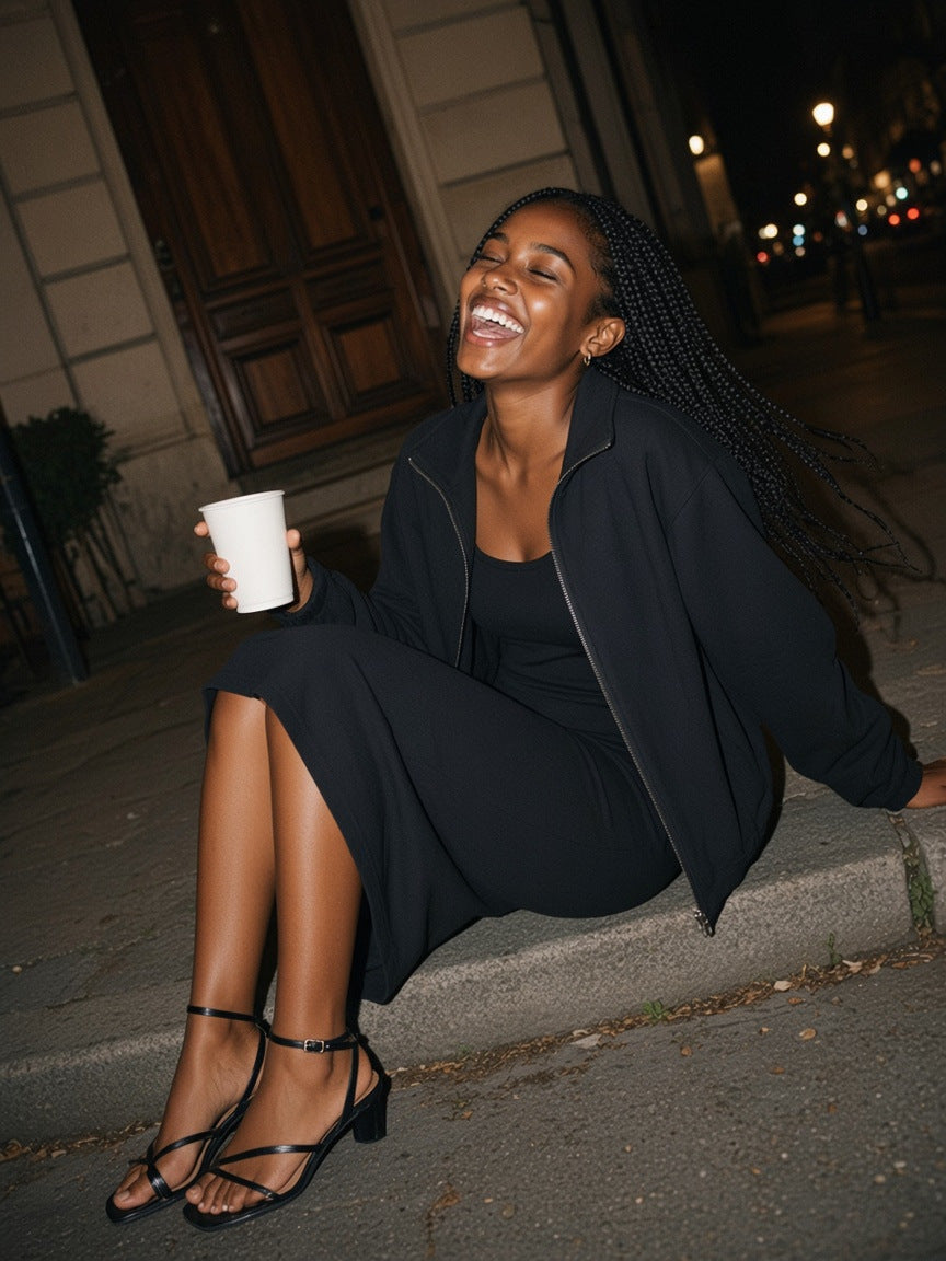 Part of the look Kerbside: woman in a black slim sleeveless dress under a black heavyweight stand-collar jacket