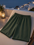 Marcel Afters Loose Raw Edge Shorts in Blackish Green, laid flat, rooftop