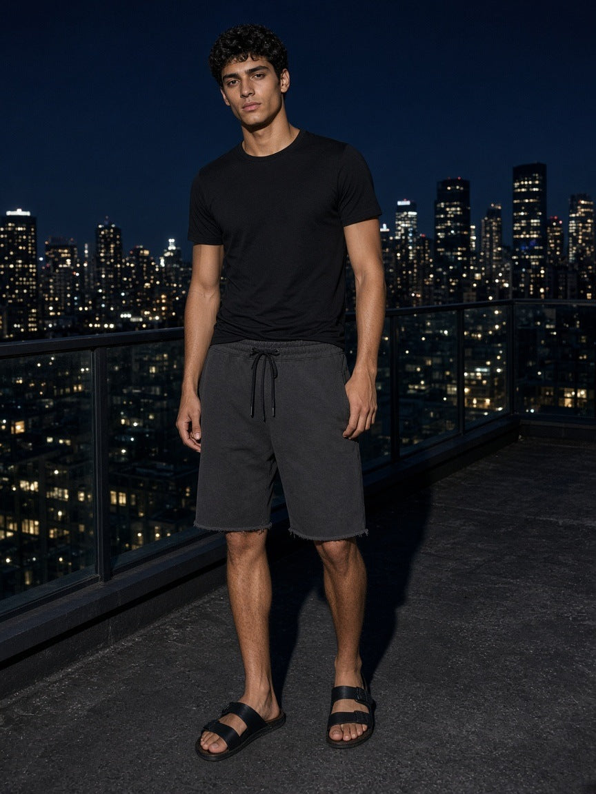 Marcel Afters Loose Raw Edge Shorts in Black, worn by a man, city rooftop at dusk