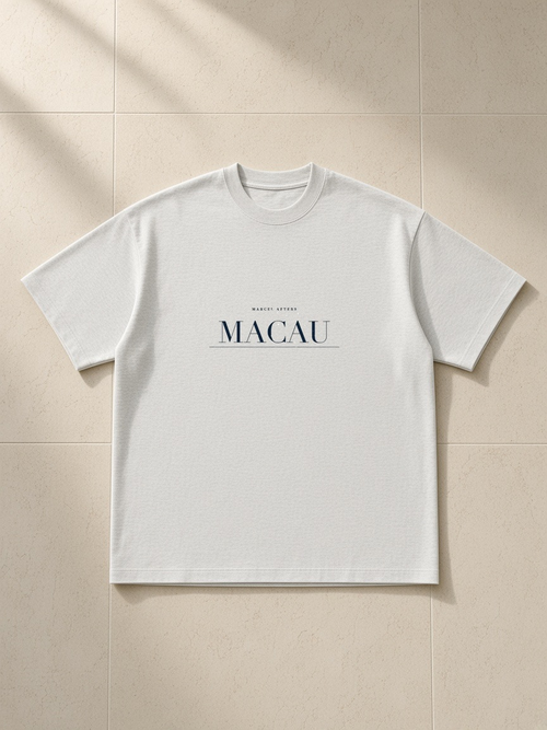 Macau heavyweight drop-shoulder tee in Oat Gray, front view with the Macau name engraved as a navy plate across the chest. Marcel Afters.
