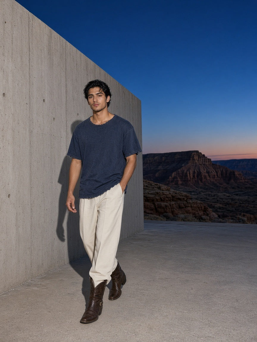 Marcel Afters Men's Heavyweight Vintage Washed Frayed T-Shirt in Navy Blue, worn by a man, walking a desert terrace at dusk in cream trousers
