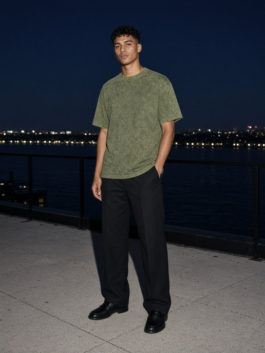 Marcel Afters Men's Snow Washed Heavyweight Oversize T-Shirt in Green, worn by a man, standing by a waterfront railing at night