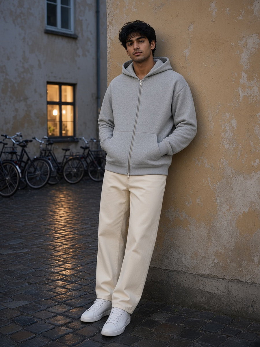 Man in the Men's Heavyweight Full Zip Hoodie in Flower Gray with ecru jeans, leaning in a Copenhagen courtyard at blue hour