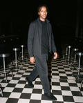 Man in Black mineral wash barrel leg pants with a black T-shirt and zip jacket, on a checkered floor at night