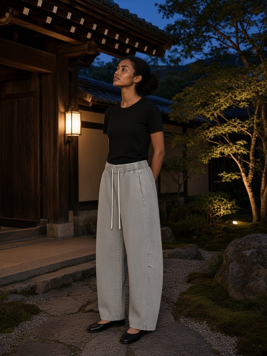 Marcel Afters Mineral Wash Barrel Leg Pants in Gray, worn by a woman, standing in a lantern-lit Kyoto garden at dusk