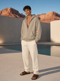 Marcel Afters Mineral Wash Boxy Full Zip Hoodie in Khaki, worn by a man, standing by a pool below red desert cliffs in cream trousers