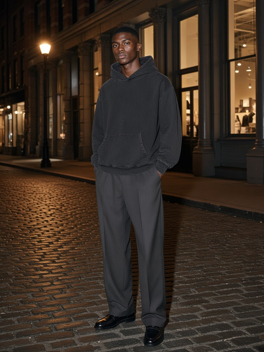 Marcel Afters Mineral Wash Oversized Hoodie in Black, worn by a man, standing on a lamp-lit cobbled street at night