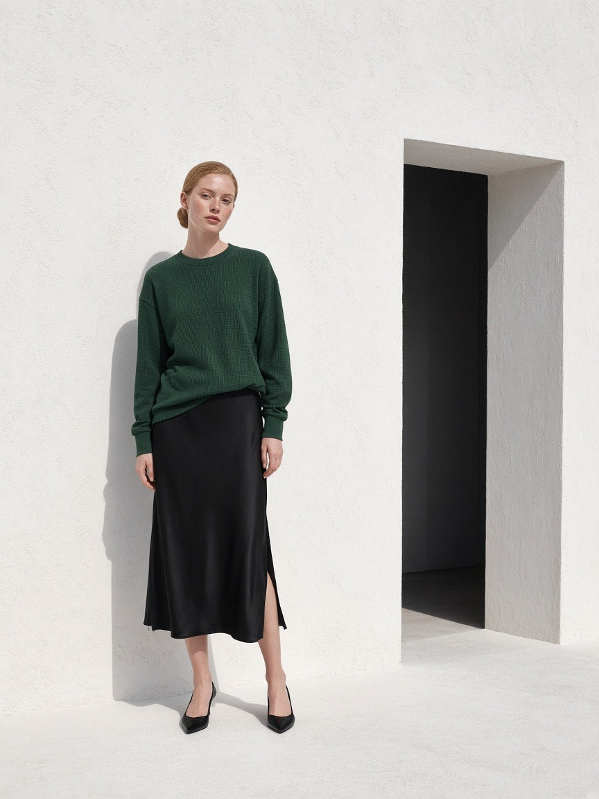 Marcel Afters Mineral Wash Waffle Oversized T-Shirt — Dark in Blackish Green, worn by a woman, standing against a white wall in a long black skirt