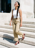 Woman wearing The One More Sandal in Wine with khaki belted barrel-leg cotton chino trousers and a white tank top, flash photograph