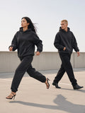 Marcel Afters Oversize Heavyweight Fleece Hoodie in Black Beauty, worn by a man and a woman, striding across a concrete rooftop, she in heels